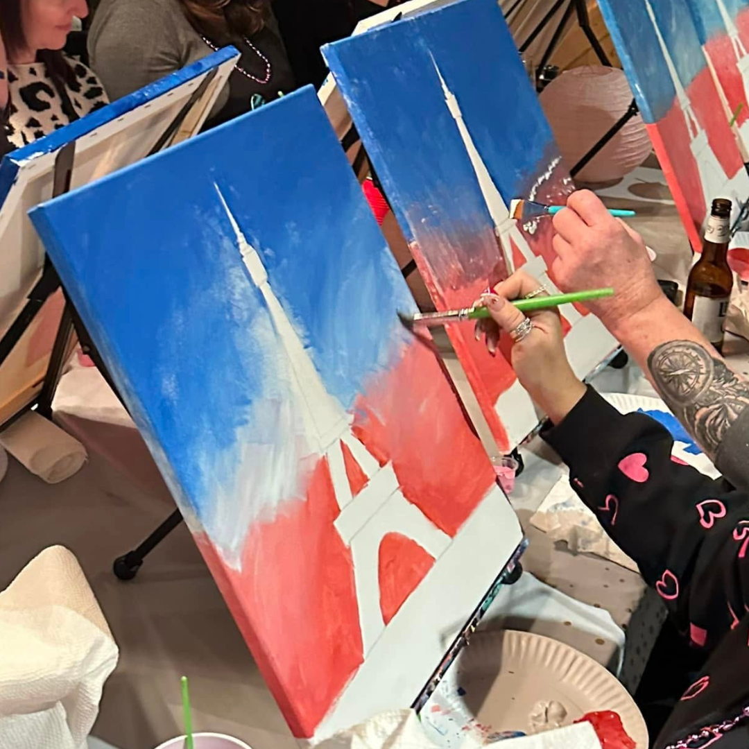 Person painting a large canvas of THE EIFFEL TOWER at a girl's trip event paint party 