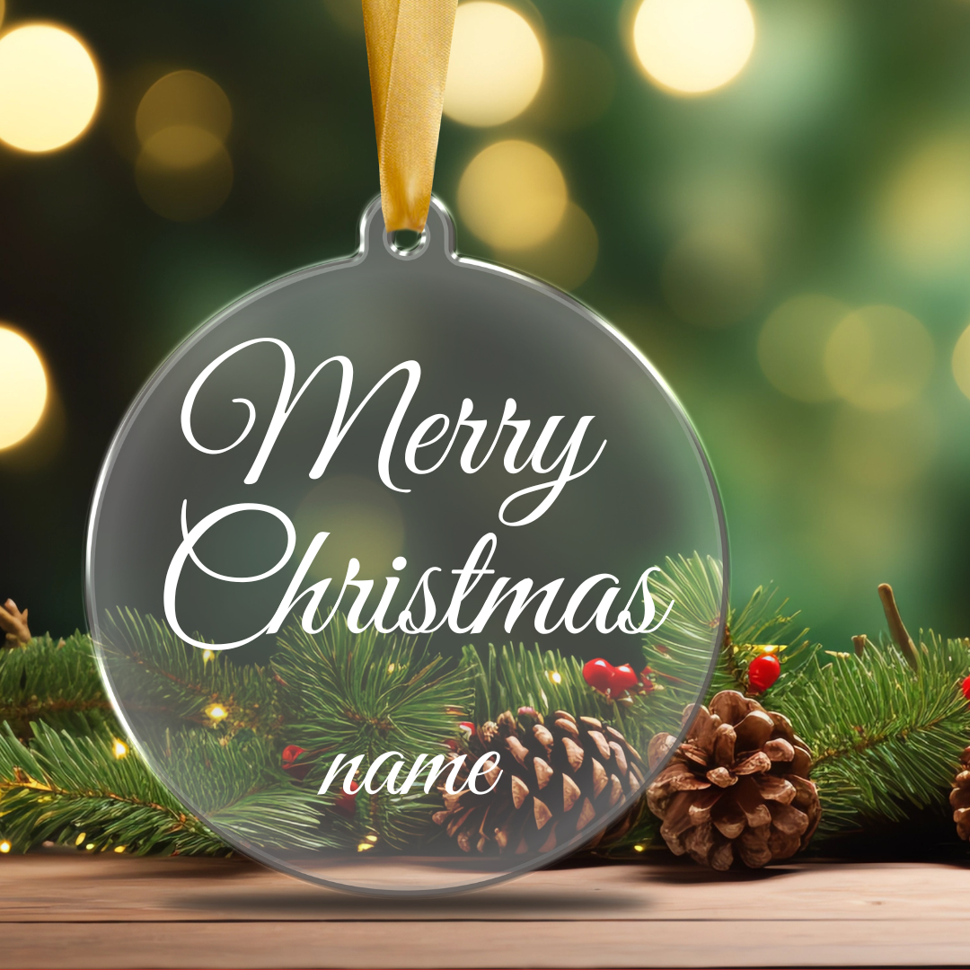A clear, flat acrylic Christmas ornament personalized Merry Christmas and name, hanging from a tree branch.