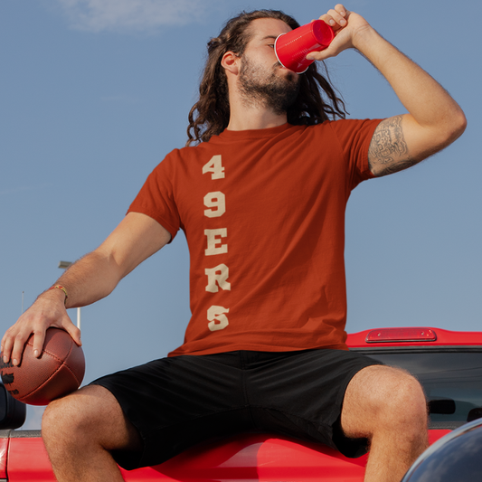 A man at a tailgate party wearing a personalized men's game day t-shirt featuring vertical gold text reading "49ERS"