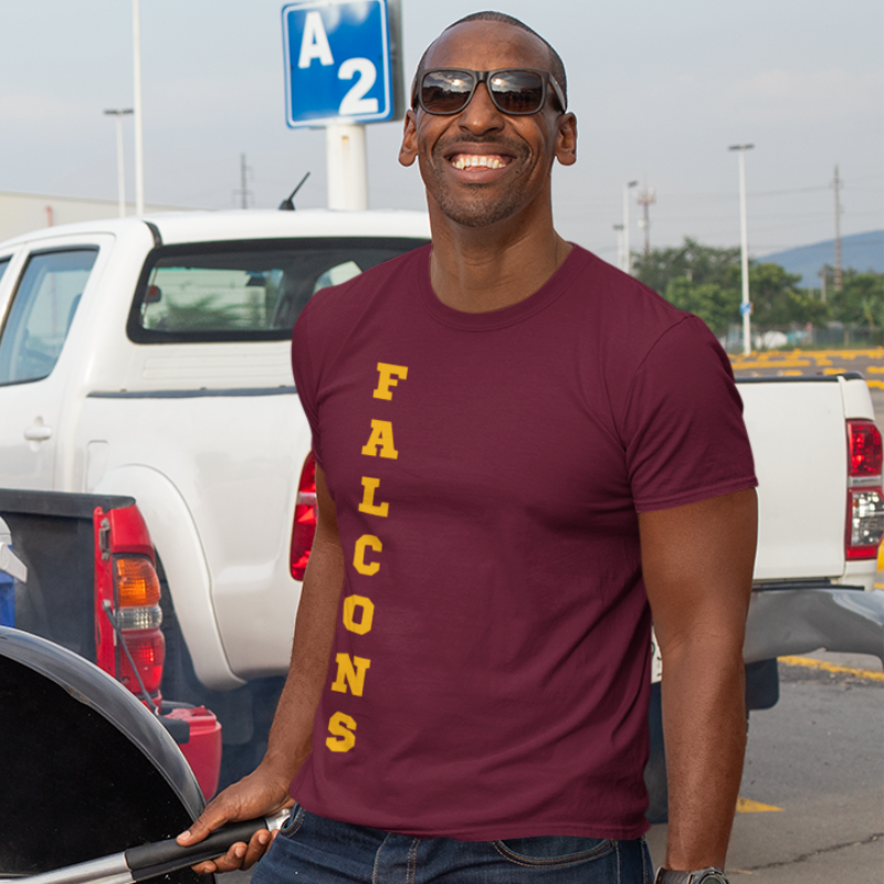 A man at a tailgate party wearing a personalized men's game day t-shirt featuring vertical gold text reading "FALCONS"