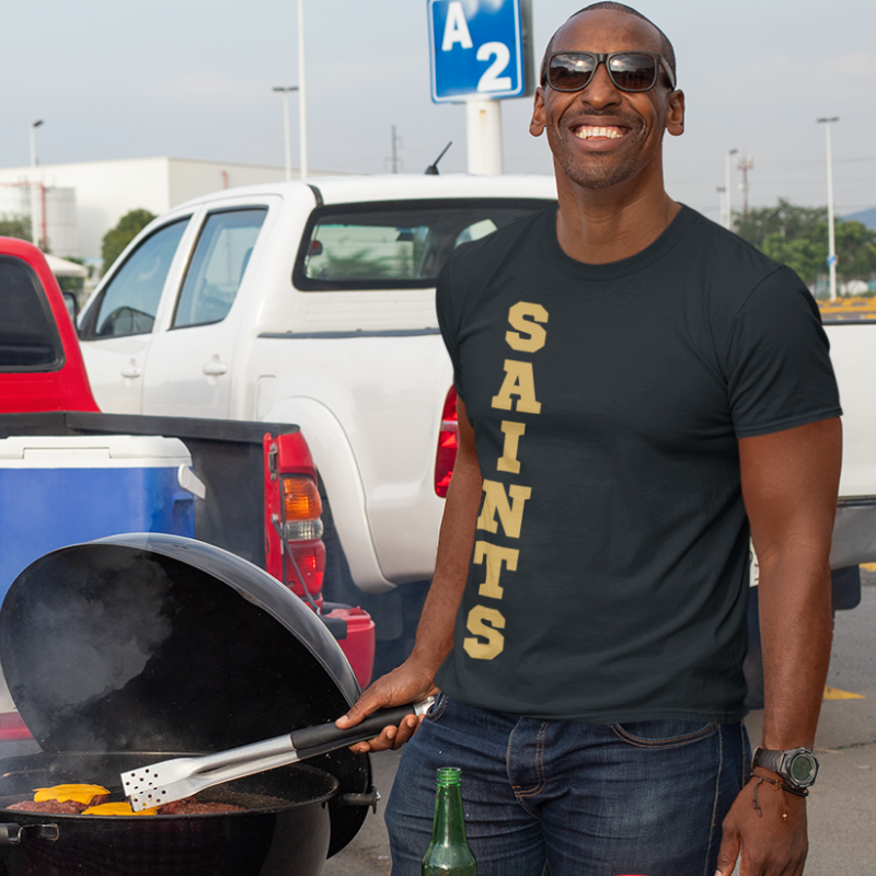 A man at a tailgate party wearing a Personalized Men's Game Day Black T-Shirt, eaturing the unique personalized team name and colors.