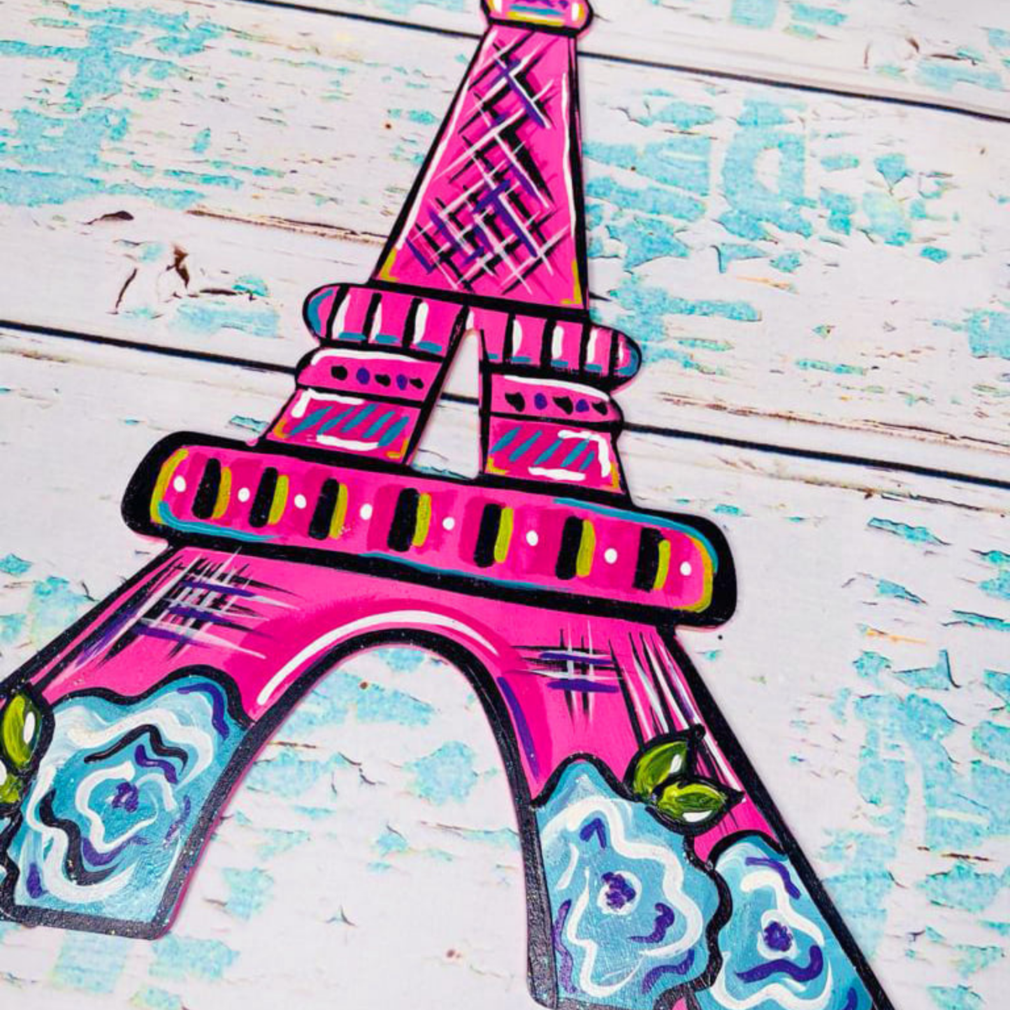 A whimsical pink Eiffel Tower decorated with blue and white flowers on a blue-tinted wood-plank background.