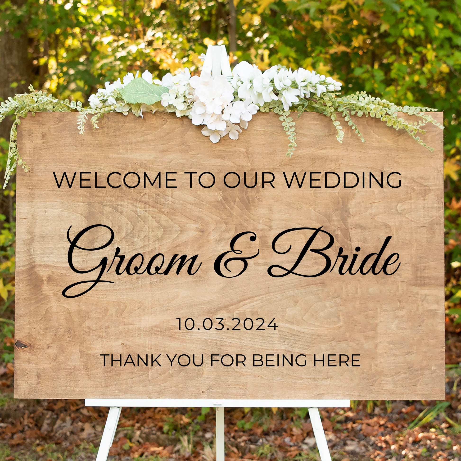 Handcrafted wooden double-sided wedding welcome sign displayed on a white easel with white florals, featuring Groom and Bride stenciled lettering.