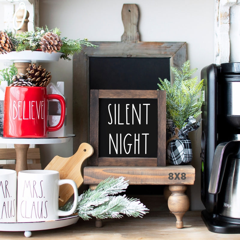 Black 8x8 Silent Night Christmas sign with white lettering and rustic wood frame displayed on a holiday kitchen shelf.