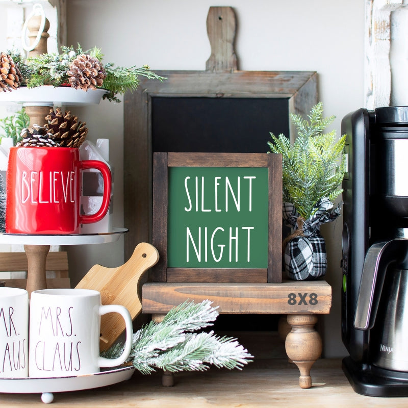 Green Silent Night Christmas sign with white lettering and rustic wood frame styled with pinecones and Christmas greenery.