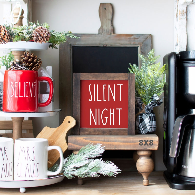 Red Silent Night Christmas tiered tray sign with white lettering and stained wood frame displayed beside festive holiday mugs.