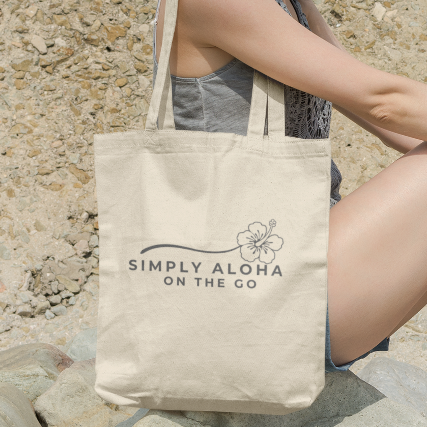 Woman relaxing on the ocean beach with a Simply Aloha On The Go™ double-sided sustainable tote bag.