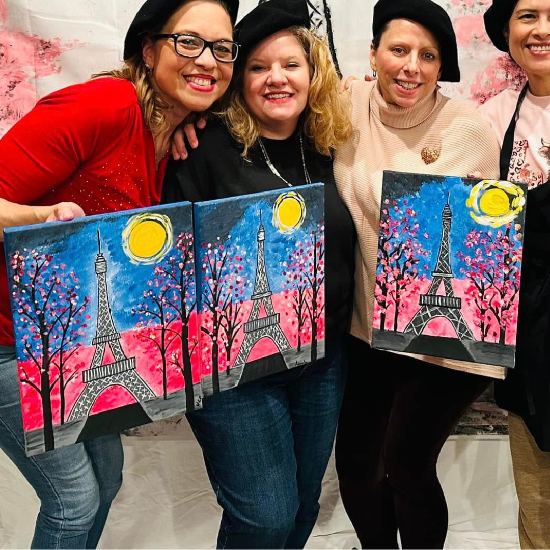 Four women holding paintings of the Eiffel Tower with cherry blossoms.
