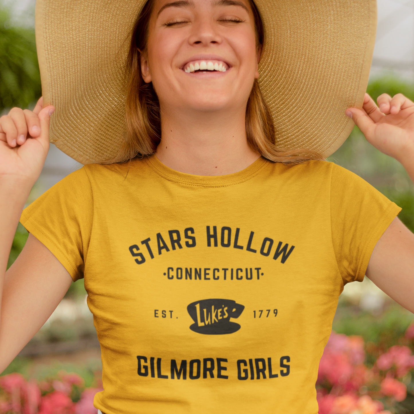 A happy woman wearing a Stars Hollow T-Shirt with the fictional town logo graphic, perfect for fans and pop culture lovers.
