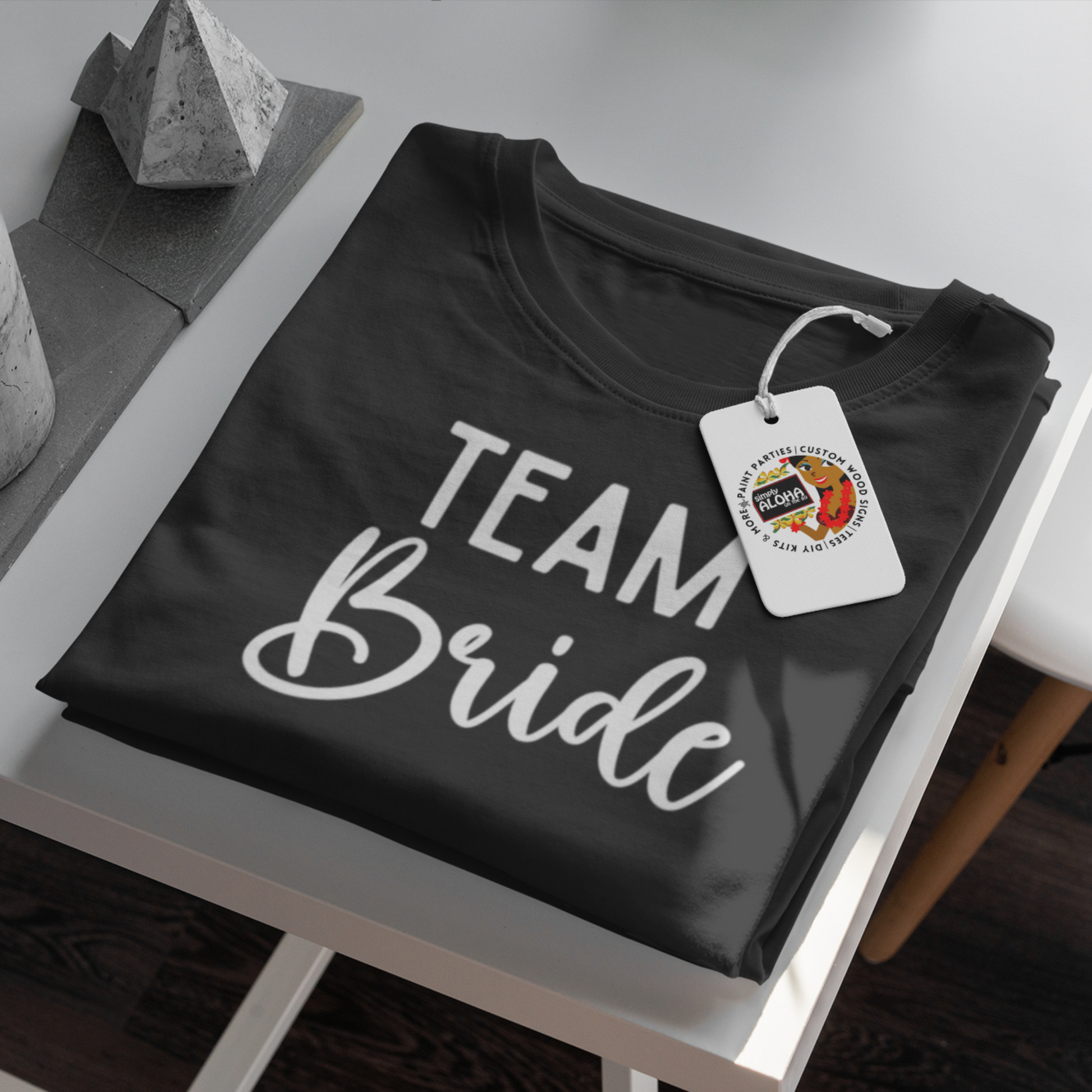 A closeup look of a clean and chic balck t-shirt with the word "Team Bride" printed in a subtle, elegant white  font. The shirt is a must-have for a bridal shower or bachelorette party