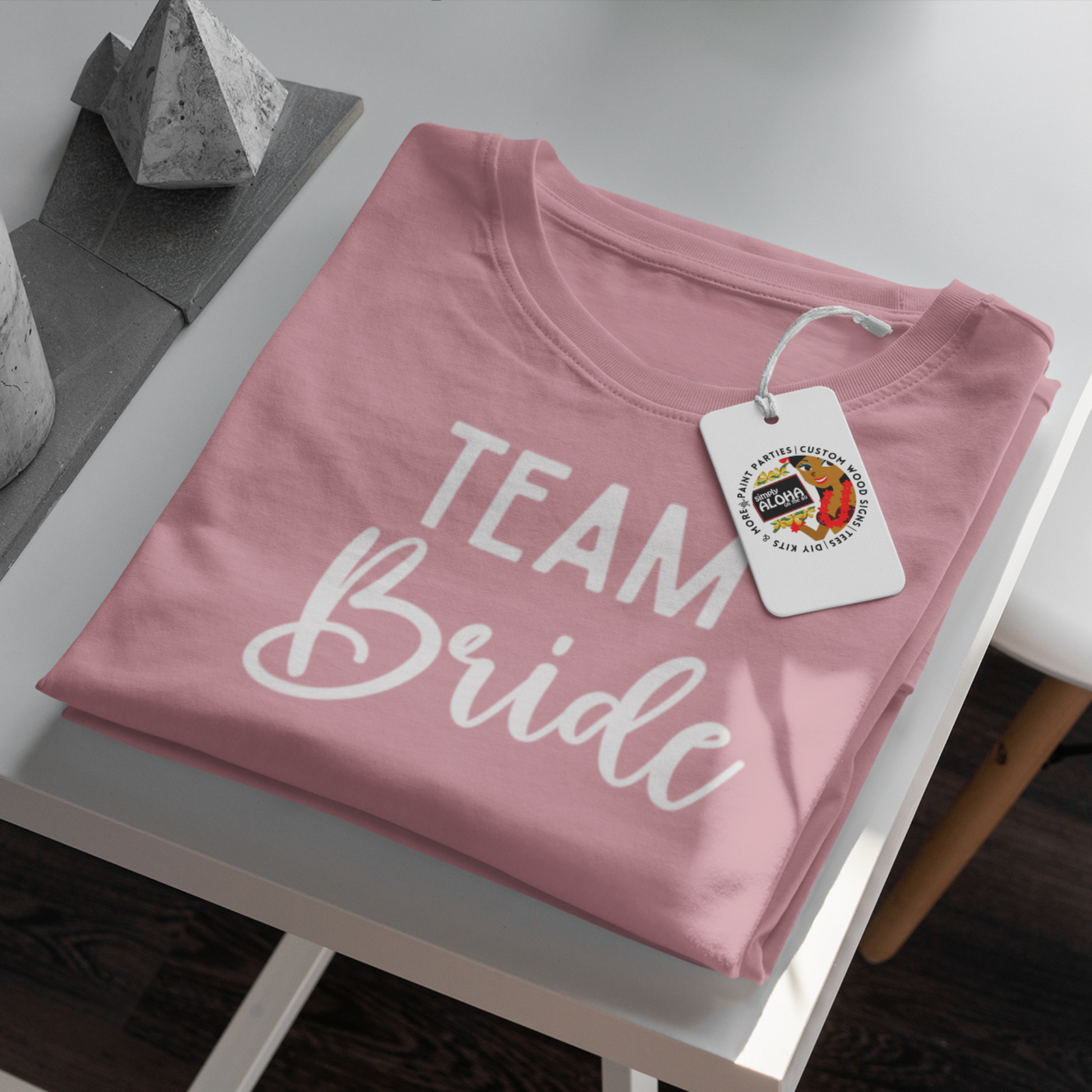 A closeup look of a clean and chic pink t-shirt with the word "Team Bride" printed in a subtle, elegant white font. The shirt is a must-have for a bridal shower or bachelorette party - Simply Aloha On the Go