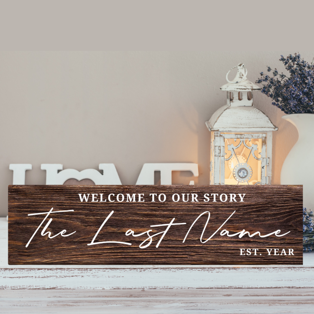 Wooden sign with "Welcome to our story The Last Name EST. YEAR" text, placed on a surface with decorative elements.