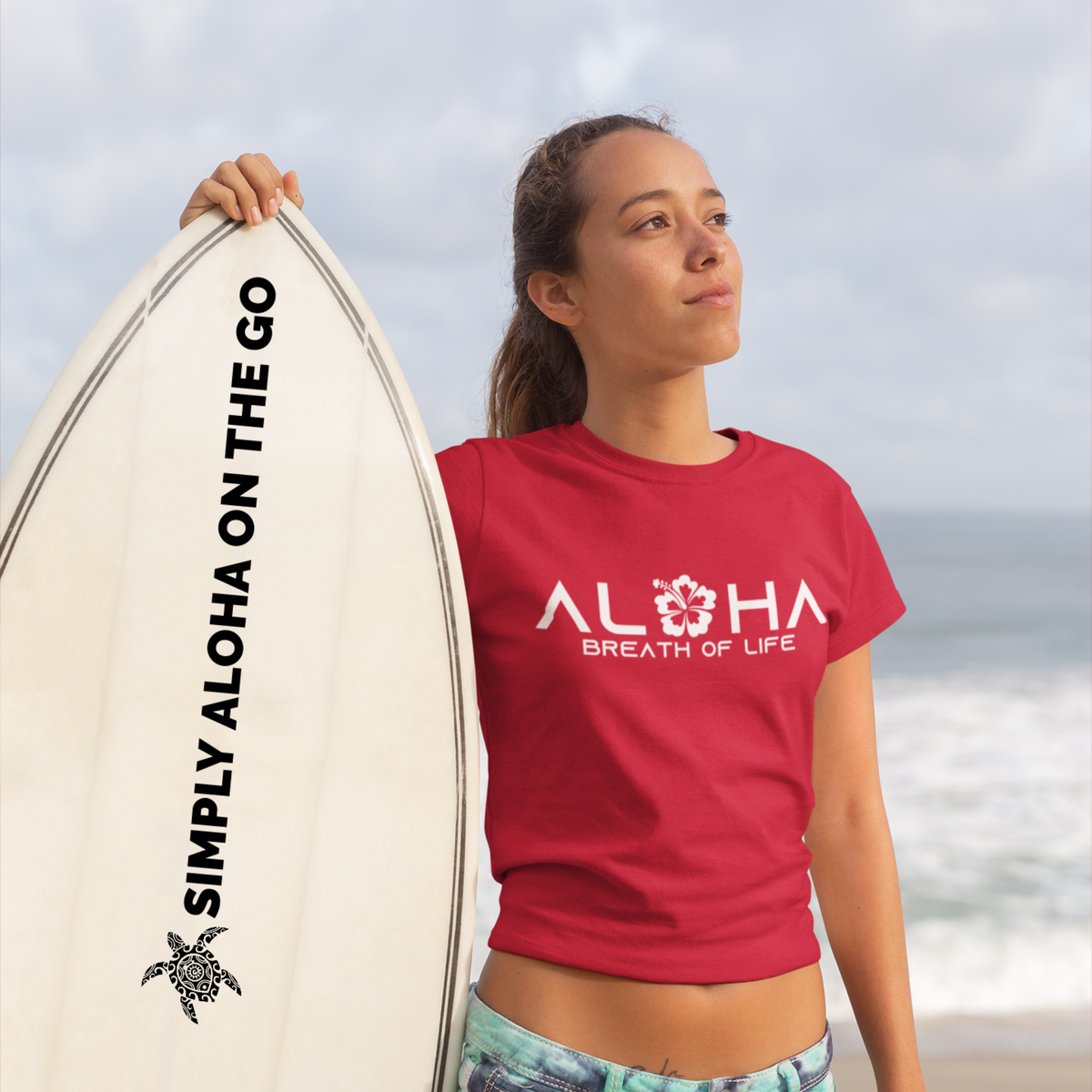 Woman wearing a red Aloha Breath of Life T-Shirt, Hawaiian-inspired tee featuring a hibiscus flower while holding a colorful surfboard.