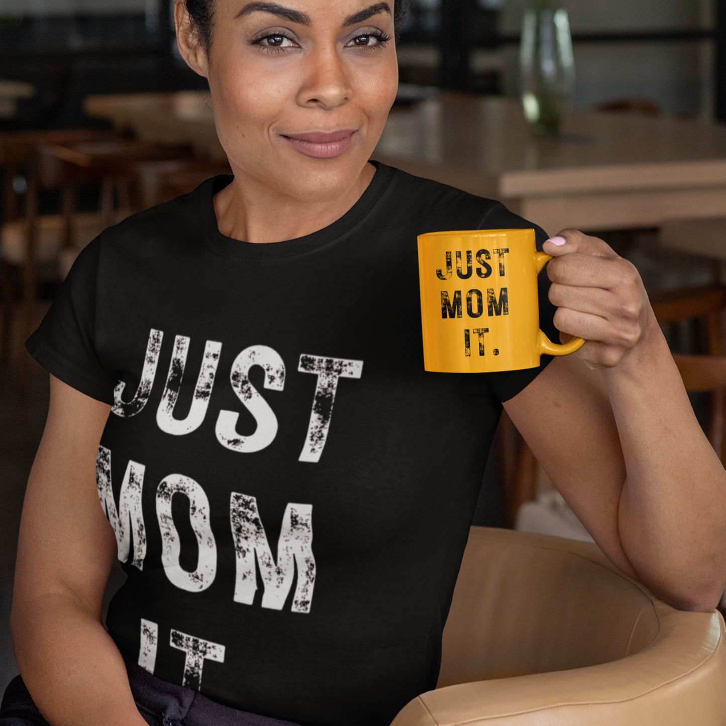 A woman wearing ablack t-shirt featuring bold white text that reads "JUST MOM IT" in a minimalist font.