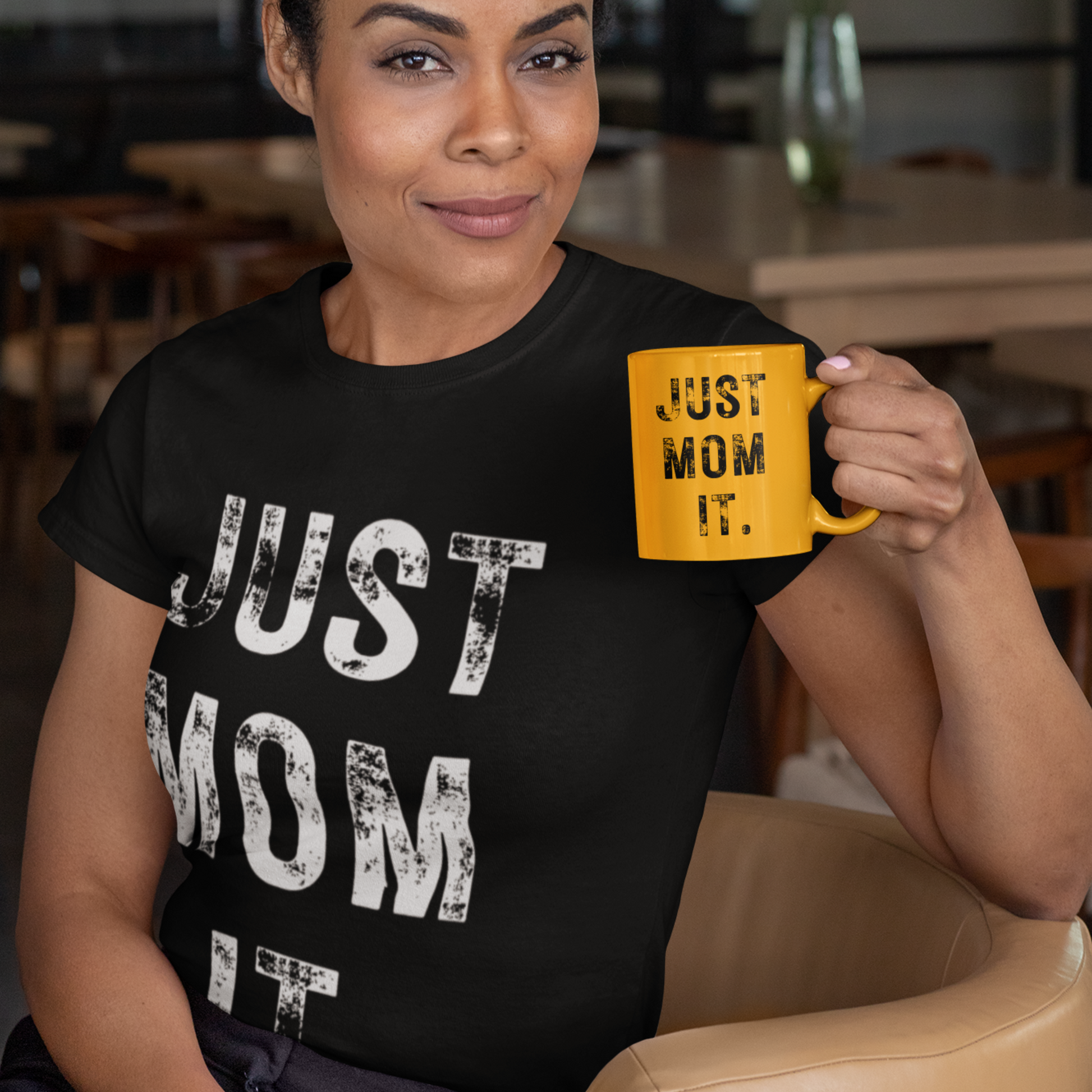 A woman wearing ablack t-shirt featuring bold white text that reads "JUST MOM IT" in a minimalist font.