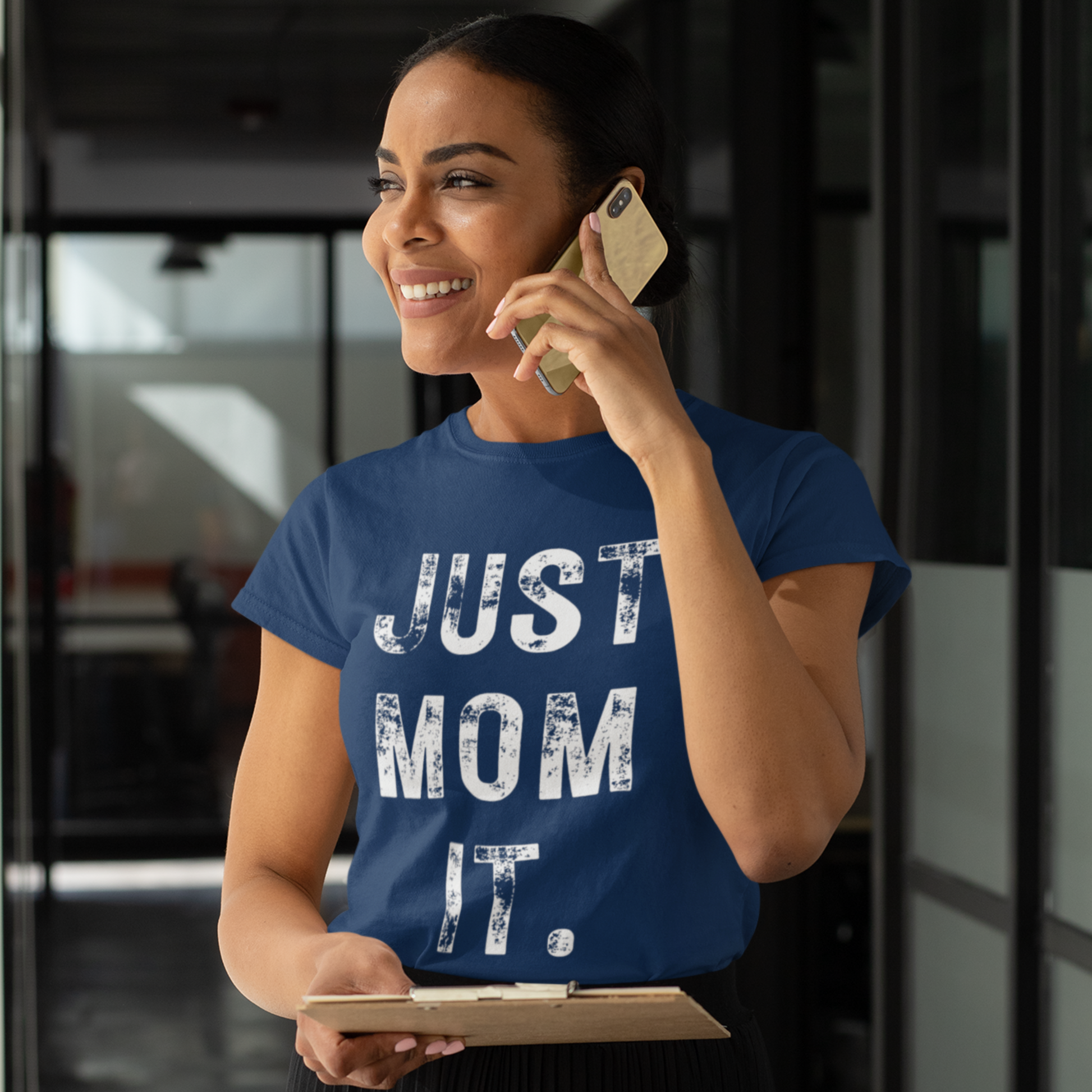 A woman wearing a bluet-shirt featuring bold white text that reads "JUST MOM IT" in a minimalist font.