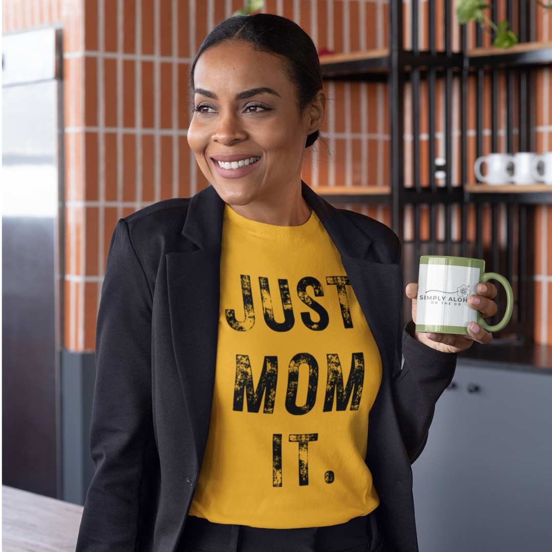 A woman wearing a gold t-shirt featuring bold black text that reads "JUST MOM IT" in a minimalist font.