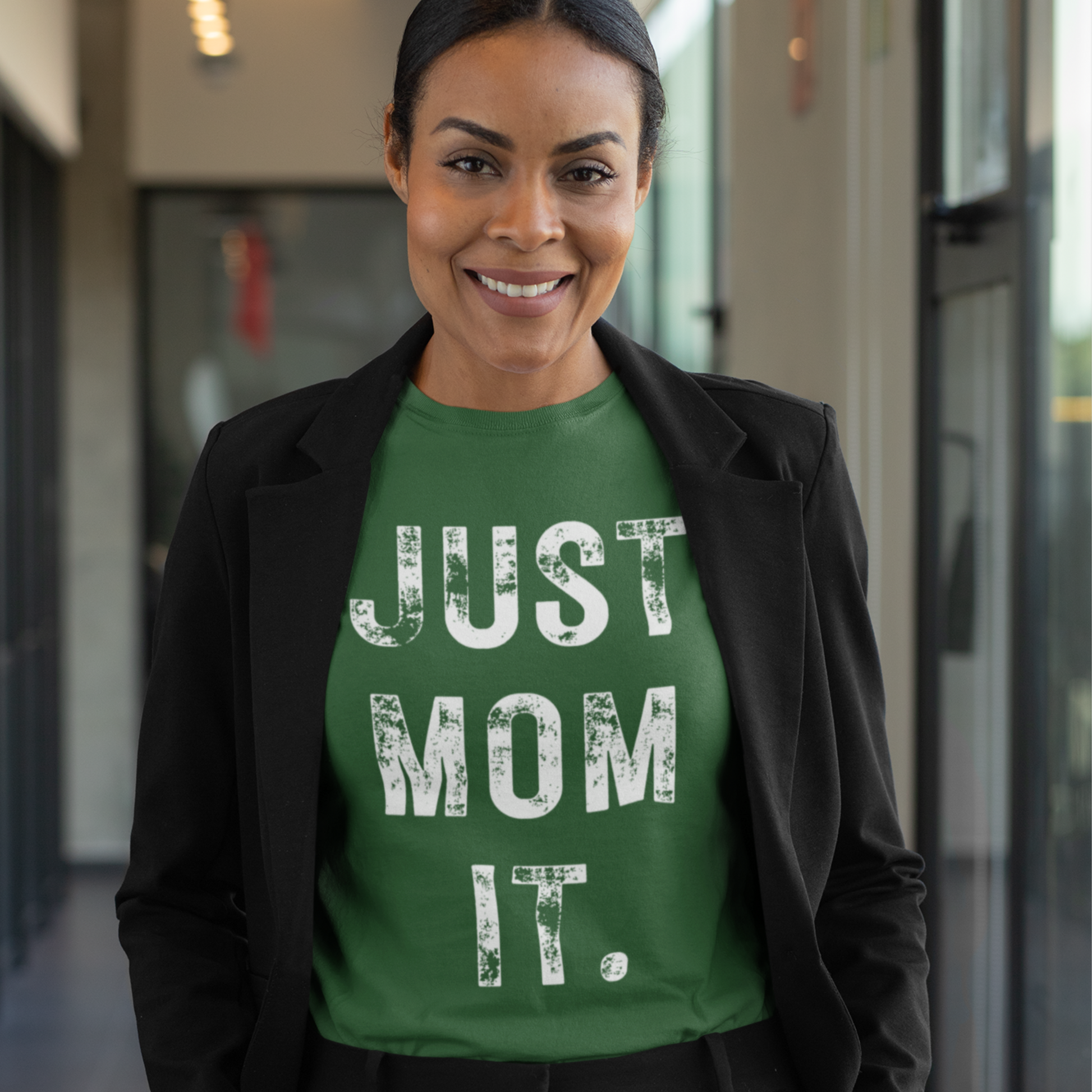 A woman wearing a green t-shirt featuring bold white text that reads "JUST MOM IT" in a minimalist font.