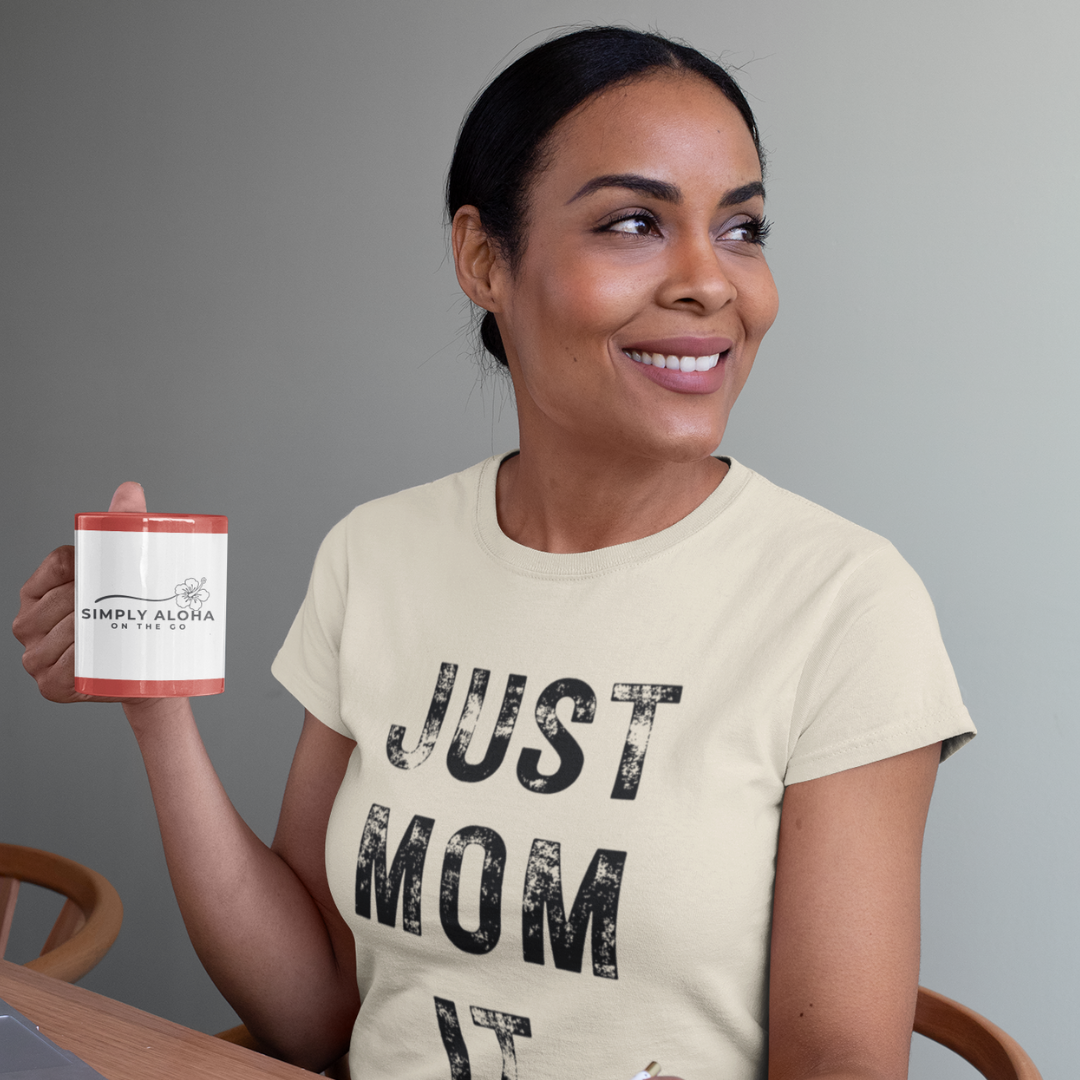 A woman wearing a sand t-shirt featuring bold black text that reads "JUST MOM IT" in a minimalist font.
