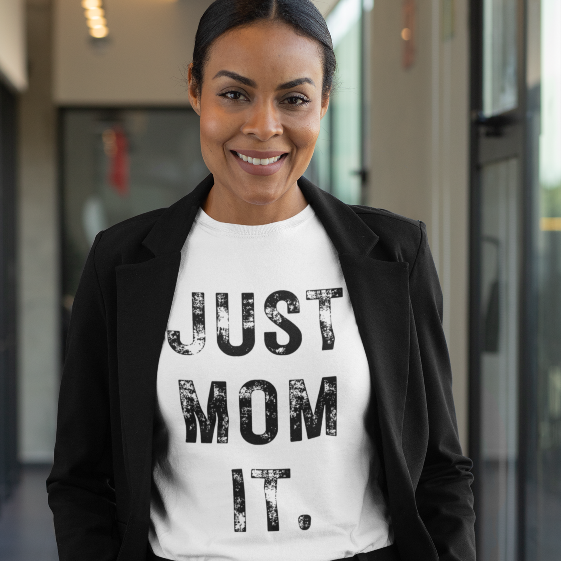A woman wearing a white t-shirt featuring bold black text that reads "JUST MOM IT" in a minimalist font.