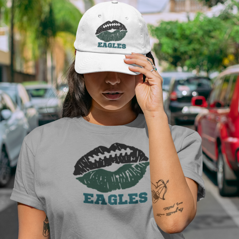 A woman wearing football game day t-shirt in grey color with a lip-themed design in midnight green and black on top and the team name Eagles written below.