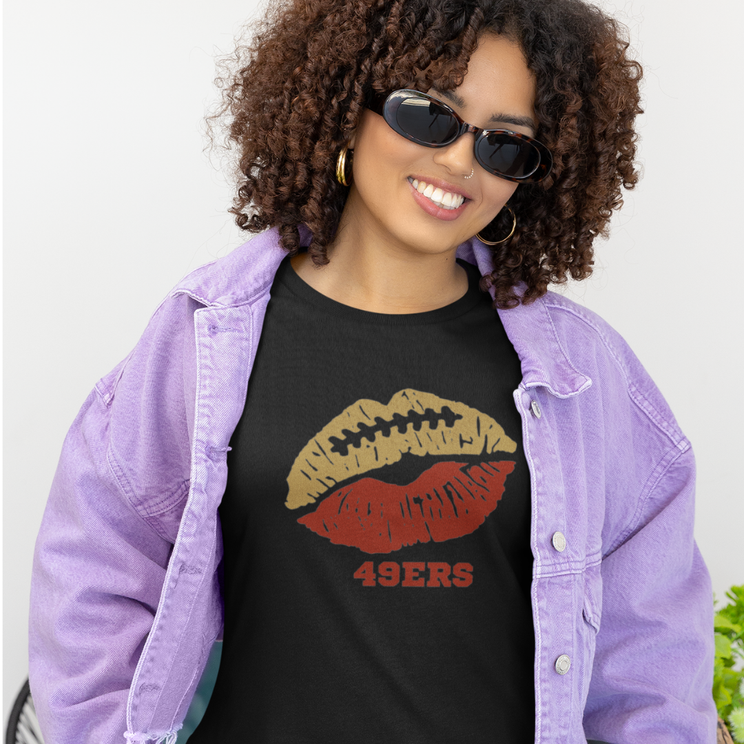 A woman wearing football game day t-shirt in black color with a lip-themed design in red and gold on top and the team name 49ers written below.