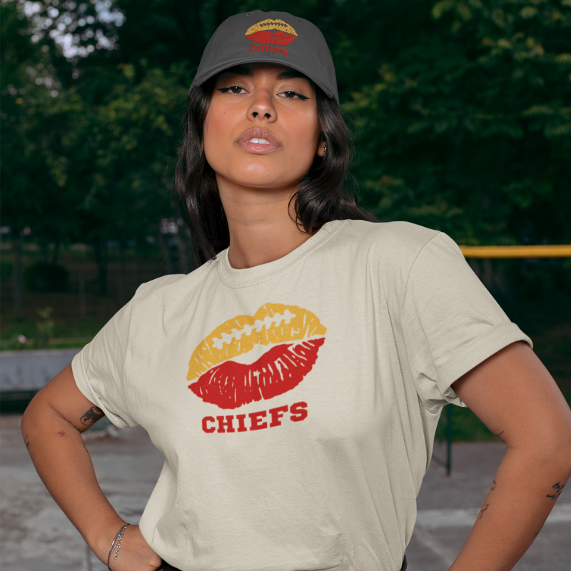 A woman wearing football game day t-shirt in cream color with a lip-themed design in blue and yellow on top and the team name Chiefs written below.