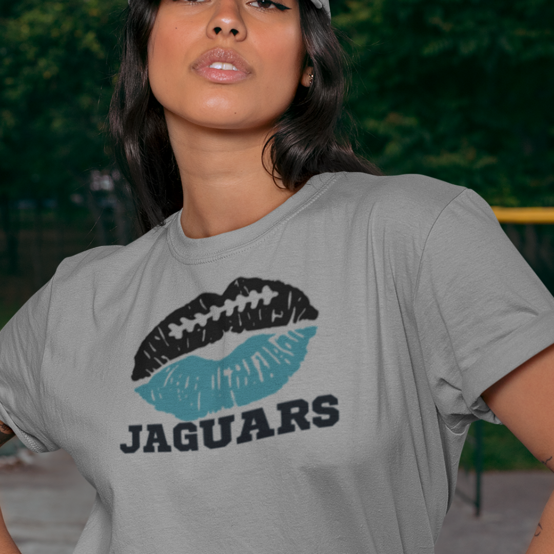 A woman wearing football game day t-shirt in grey color with a lip-themed design in black and teal on top and the team name Jaguars written below.