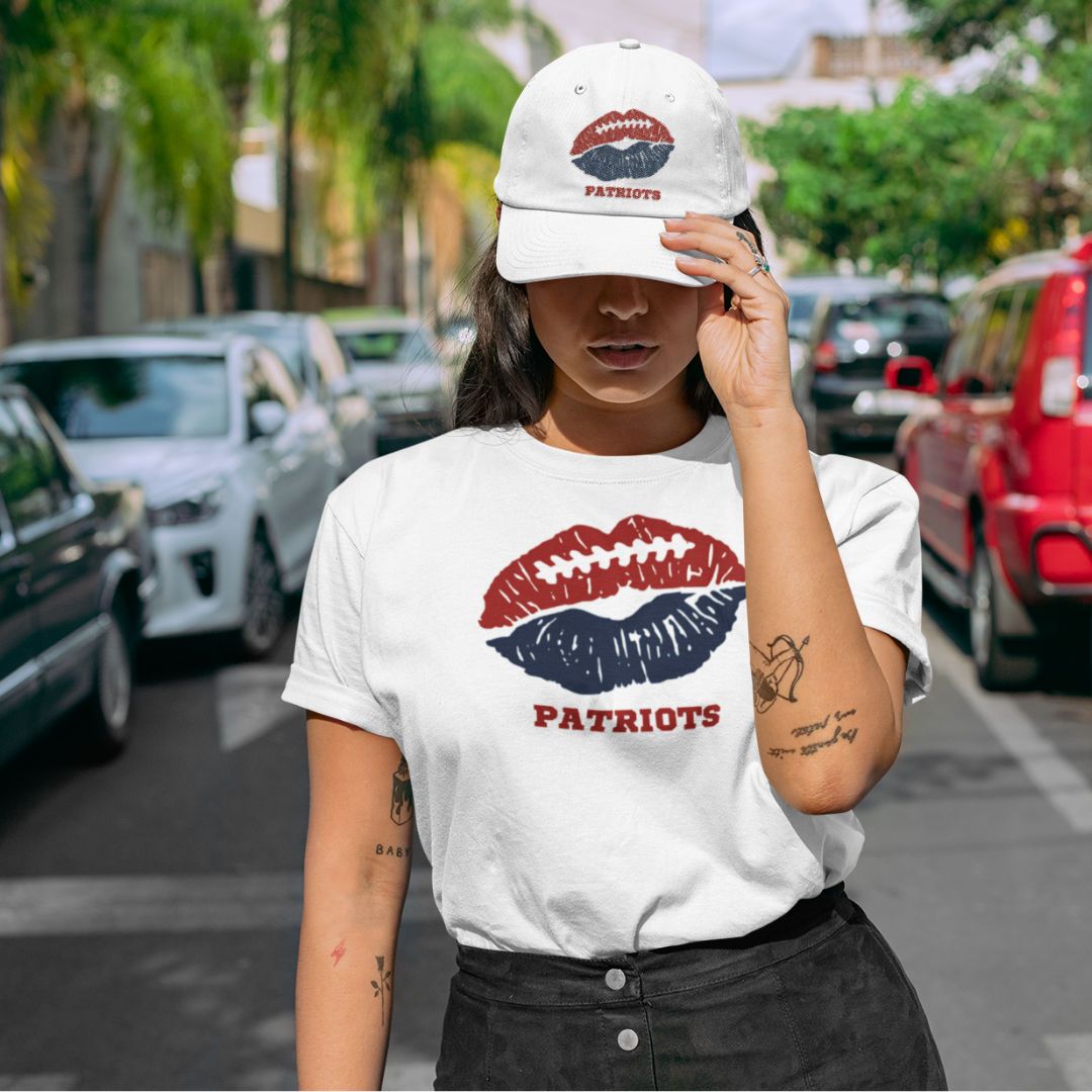 A woman wearing football game day t-shirt in white color with a lip-themed design in nautical blue and red on top and the team name Patriots written below.