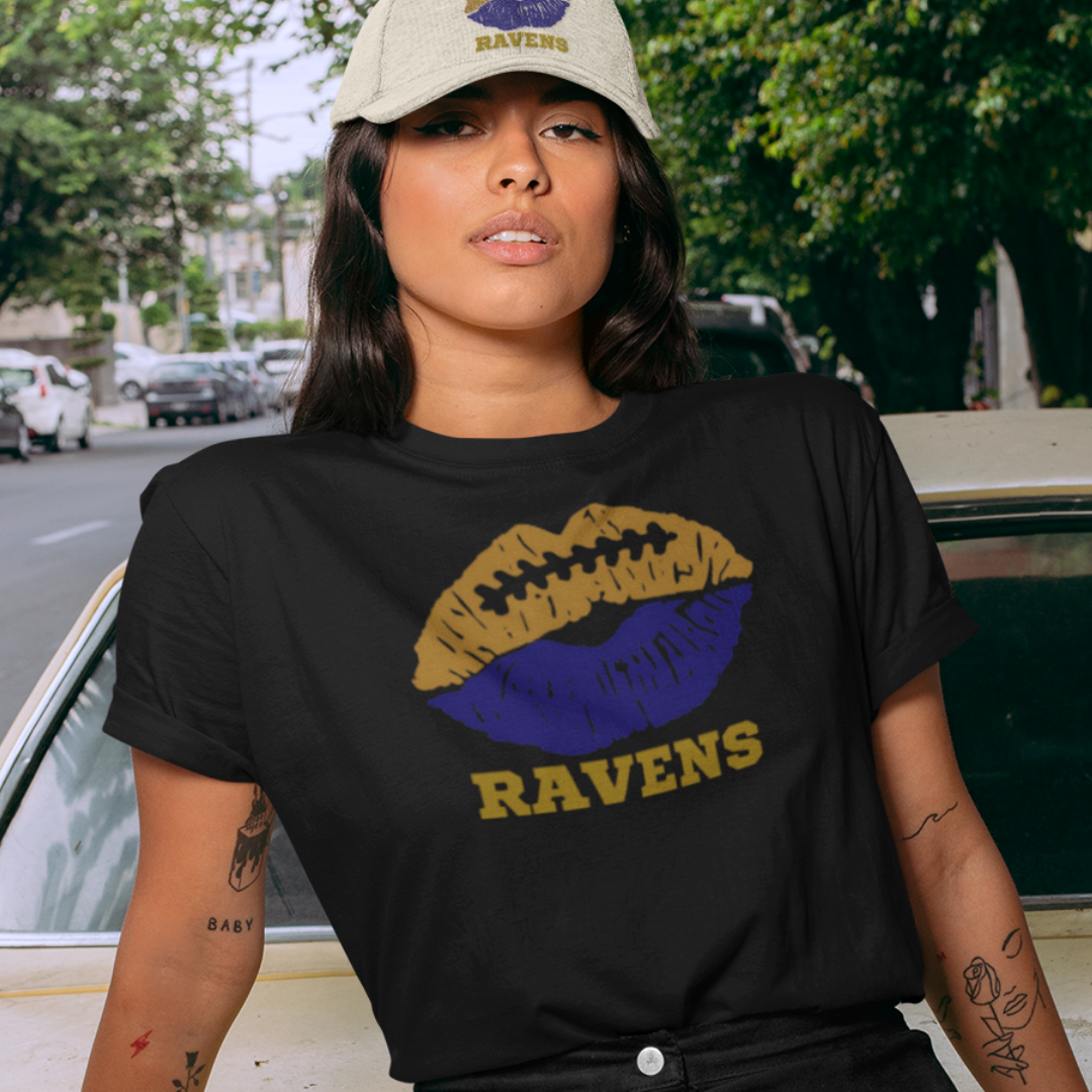 A woman wearing football game day t-shirt in black color with a lip-themed design in deep purple and black on top and the team name Ravens written below.