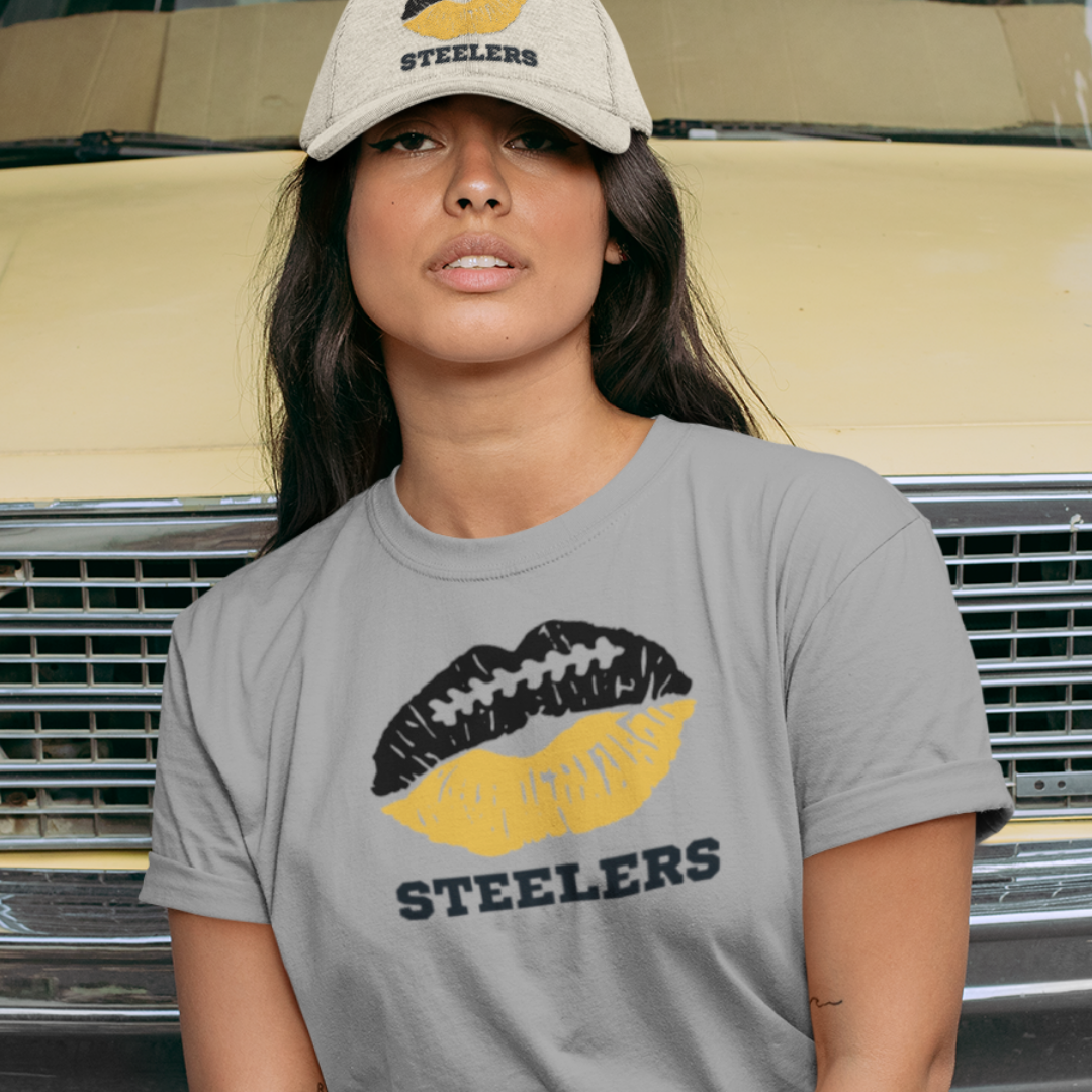 A woman wearing football game day t-shirt in grey color with a lip-themed design in black and gold on top and the team name Rams written below.