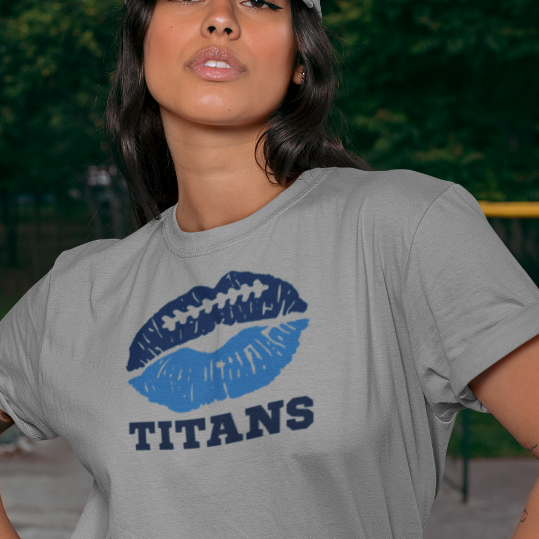 A woman wearing football game day t-shirt in grey color with a lip-themed design in Titans blue and navy on top and the team name Titans written below.